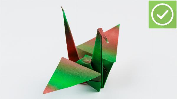 Gấp giấy origami bước đầu tiên: Cắt đôi tờ giấy vuông, sau đó gấp đôi theo chiều dọc và chiều ngang, rồi mở ra để lộ các nếp gấp.